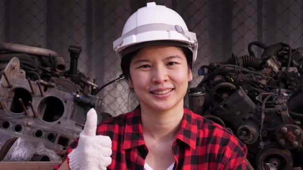 Asian female industrial worker in putting on a hard hat, putting the thumb up