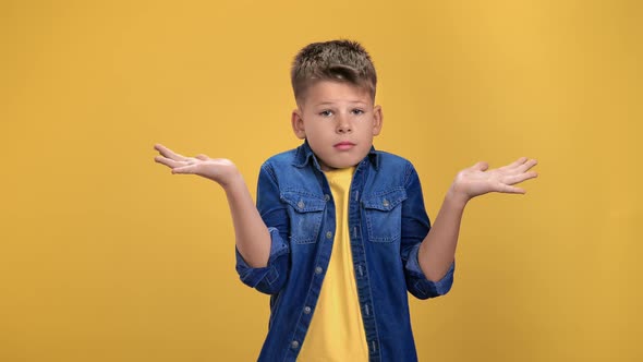 Helpless Boy Kid Showing Gesture Dont Know Guilty Face Expression Posing Isolated on Orange Studio