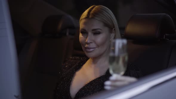 Portrait of Elegant Positive Young Woman Raising Glass with Champagne and Smiling at Camera. Stylish