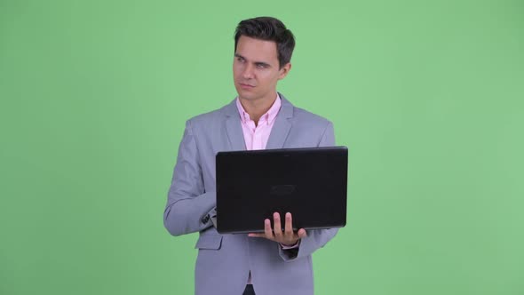 Happy Young Handsome Businessman Thinking While Using Laptop