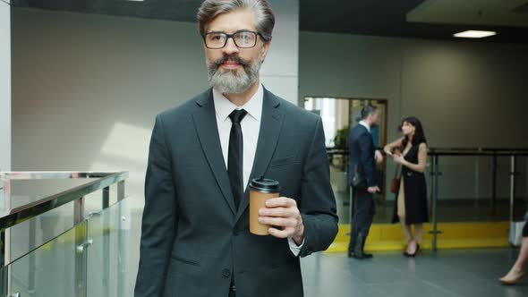 Portrait of Mature Man in Suit Walking in Office Building Hallway with Take Out Coffee