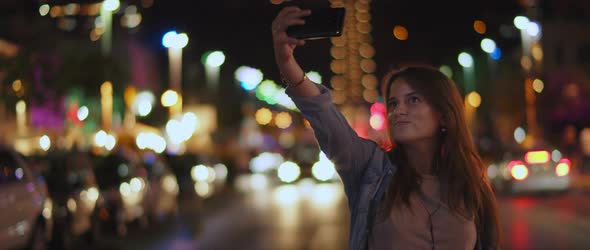 A young woman taking a selfie in the middle of the street, bokeh lights