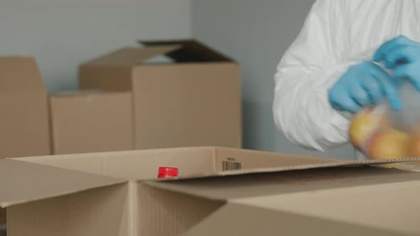 A Person in Protective Gloves Packs Food Into a Cardboard Box