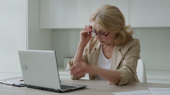 Tired Frustrated Elderly Woman Takes Off Her Glasses Takes a Break From Working at Her Laptop