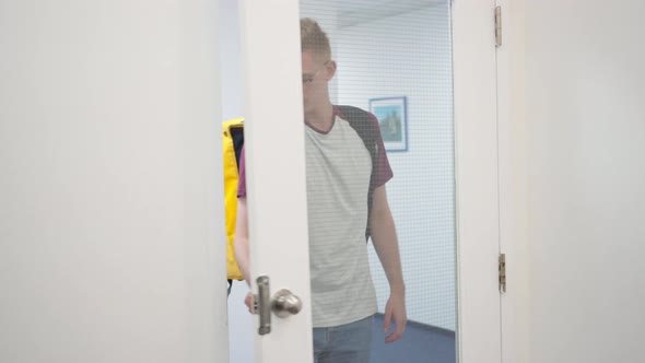 Confident Young Male Courier Walking to Elevator in Business Center with Yellow Insulated Bag