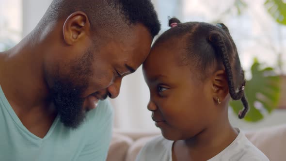 Lovely Black Father and Little Daughter Cuddling Sitting on Couch at Home