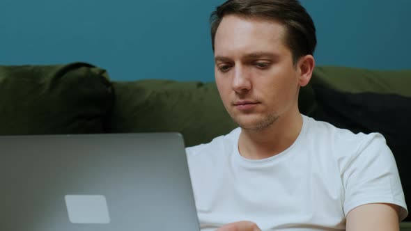 Young Man Sitting Near Sofa with Laptop Working From Home Concept