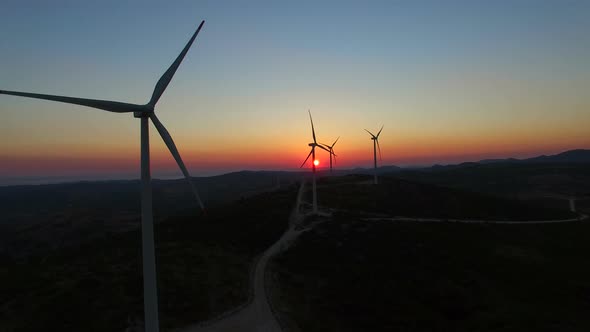 Aerial view of slowly rotating windmill blades at colorful sunset alt