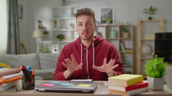 A Young Man Sitting at a Desk at Home Talks to the Camera