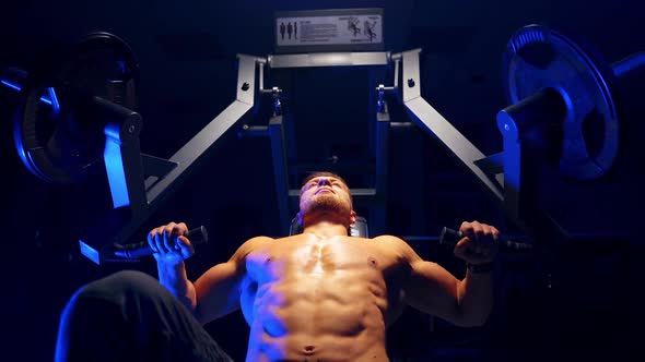 Handsome young man doing bench press workout in gym. Blue light filter. Strong abs. Heavy lift.