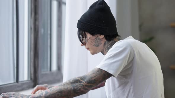 Side View Stressed Tattooed Man Thinking Looking Out the Window Standing Indoors