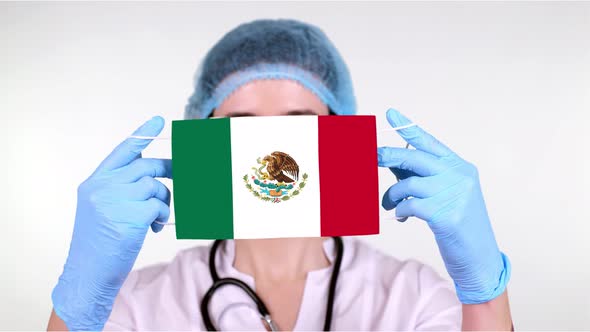 Close-up. Doctor in Glasses, Blue Medical Cap, Gloves Holds in Hands Medical Mask with Mexico Flag