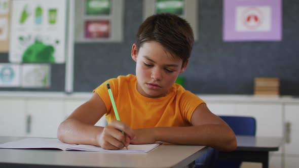 Portrait of happy mixed race schoolboy sitting at classroom, making notes, looking at camera