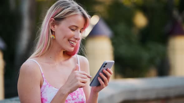 A pleased woman with rainbow earrings using her phone during pride gay parade