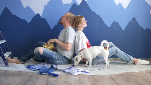 a man and woman with a dog sit back against a wall with a picture of mountains