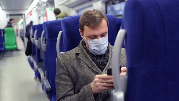 Millennial Man in Mask Commuting on Train Sitting Listening to Music on Mobile Phone