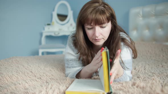 Pretty Woman Lies on the Bed Opens a Book and Starts Reading