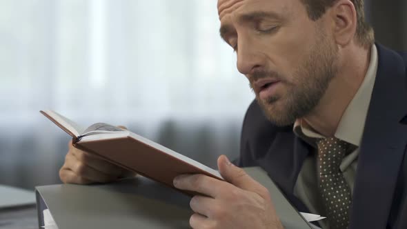 Sleepy overworked office worker trying to read report at workplace, overtime