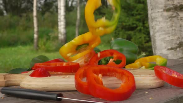 Slices of Fresh Pepper Fall on a Wooden Board