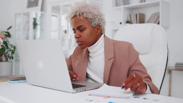 African American Woman Office Worker Typing on Laptop and Notes in Notepad