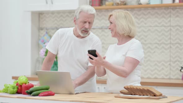 Old Couple Working on Laptop &amp; Smartphone in Kitchen
