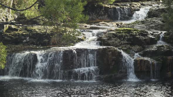 A small multi-level waterfall behind some branches on a sunny day, tight shot