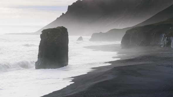 Misty Black Sand Beach With Sea Stack And White Surf