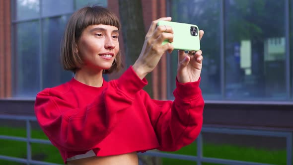 Cute Millenial Girl in Red Cropp Sweater Doing Photos on Her Phone on the Street