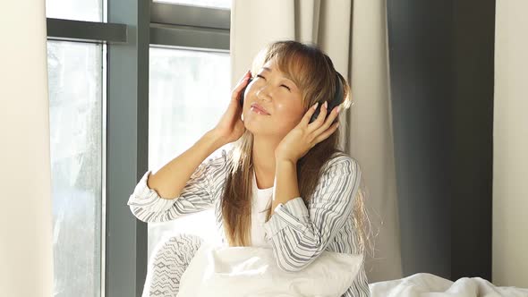 Portrait of a Beautiful Smiling Woman Dressed in Pajamas and Listening To Music with Headphones