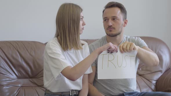 Man and Woman Tearing Apart the Word Trust Written on the Paper