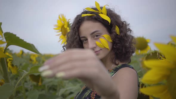Portrait of Beautiful Curly Girl Inviting, Attracting Viewer in the Sunflower Field