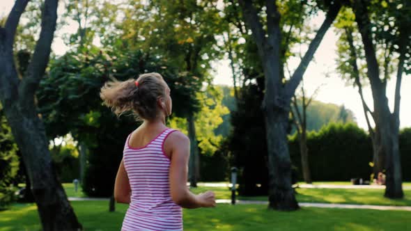 An Attractive Woman Jogs in the Park. Listening To Music on Headphones.