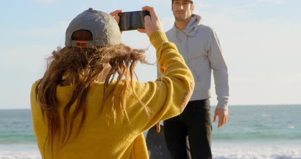 Rear view of young caucasian woman clicking photo of young caucasian man with camera on the beach 4k