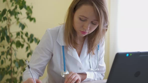 A nurse in a bathrobe and with a stethoscope works at a laptop