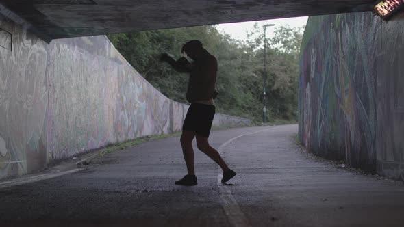 Wide Shot of a Young Athletic Man Boxing in an Underpass, Silhouetted By The Light Behind Him - Ungr