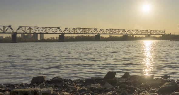 Timelapse of City River Bank. Sun Rays, Blue Sky and Railway Bridge Over Horizont. Summer Sunset