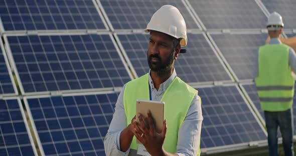 Male Worker Looking at Tablet Screen and Than Aside. Man in Hard Helmet and Uniform Standing at