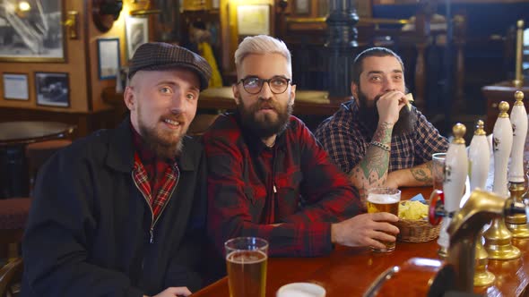 Male Friends Drinking Beer and Eating Snack in Sports Bar