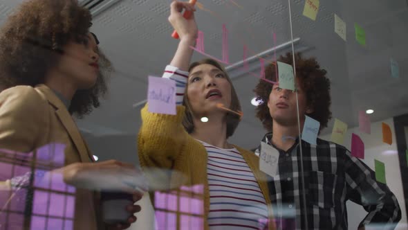 Diverse work colleagues using memo notes and writing on glass wall having a discussion