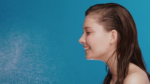 Fresh Girl with Perfect Clean Skin Getting Water Spalshes and Smiling on Blue Background