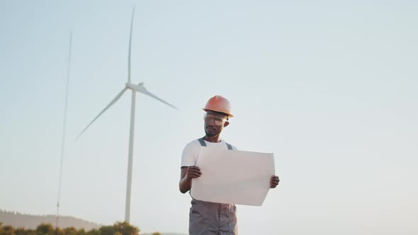 Focused African American Man with Blueprints in Hands Standing Among Farm with