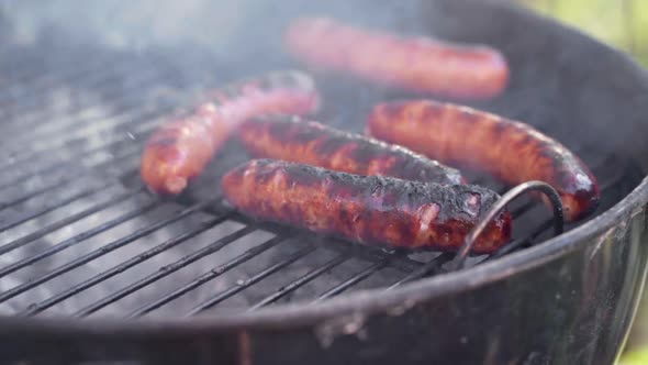 Slow Motion of Tongs Picking Up Gristly Sausages From a Smokey BBQ Grill