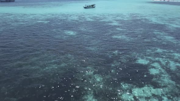 Aerial drone shot over some boats sailing through the sea in an idyllic turquoise seascape with an i