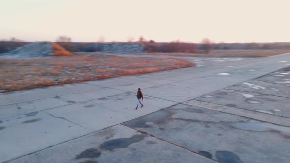 Camera Rotates Around Bearded Man Walking Along Concrete Road for Planes at Bright Winter Sunset