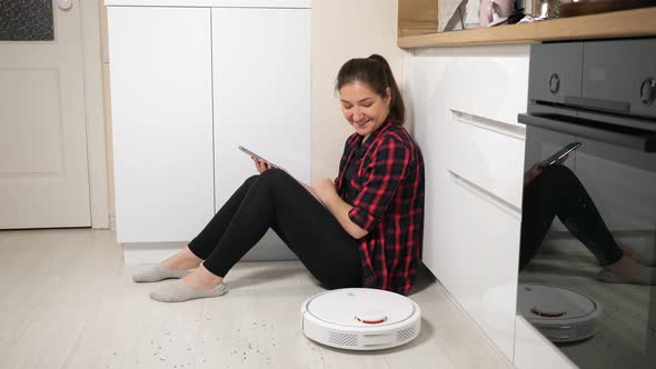 Woman with Phone Looking at Robot Vacuum Cleaner on Floor