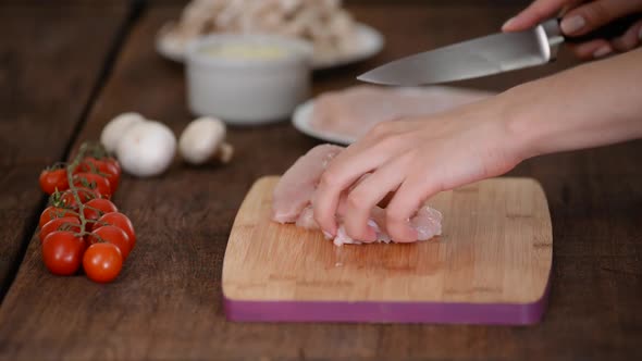 Female hands cutting chicken fillet on wooden chopping board