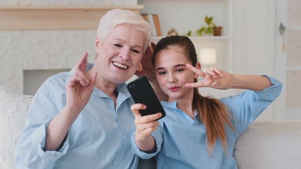 Funny Elder Mature Grandma and Little Granddaughter Bloggers Having Fun Video Calling on Smartphone
