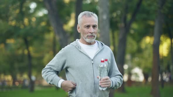Active Grandfather Drinking Water After Workout in Park