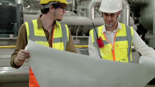 Engineerc and Foreman are discussing the plant layout on the blueprint in the factory boiler room