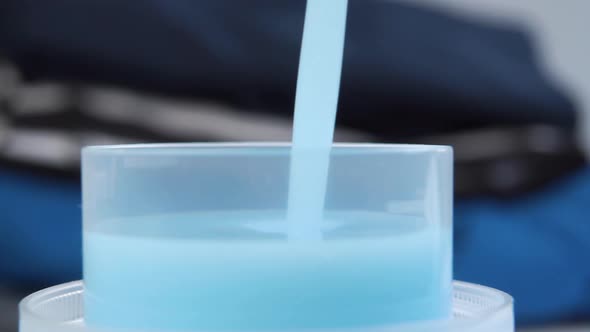 Macro shot of pouring blue liquid laundry detergent into a plastic measuring cap